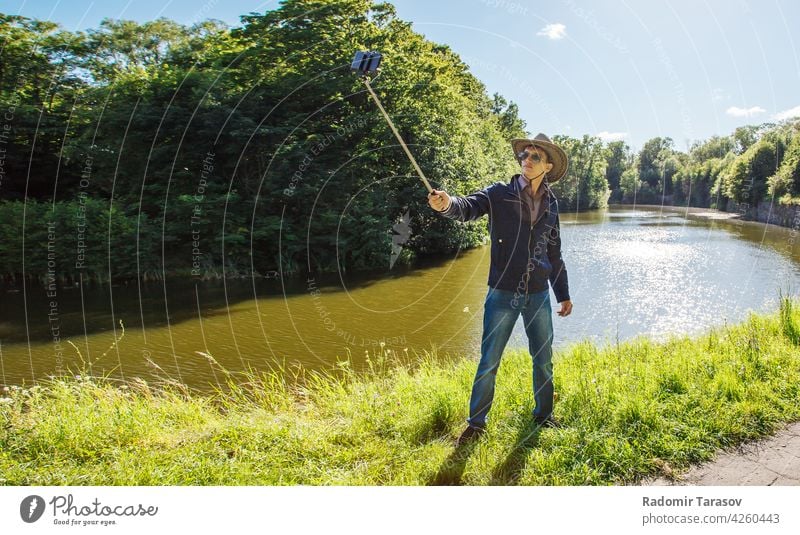 junger Mann macht Selfie mit einem Selfie-Stick Sommer kleben Fotokamera Selbst Gesicht Porträt Glück Park Hintergrund Person machen Smartphone Hand Fotograf