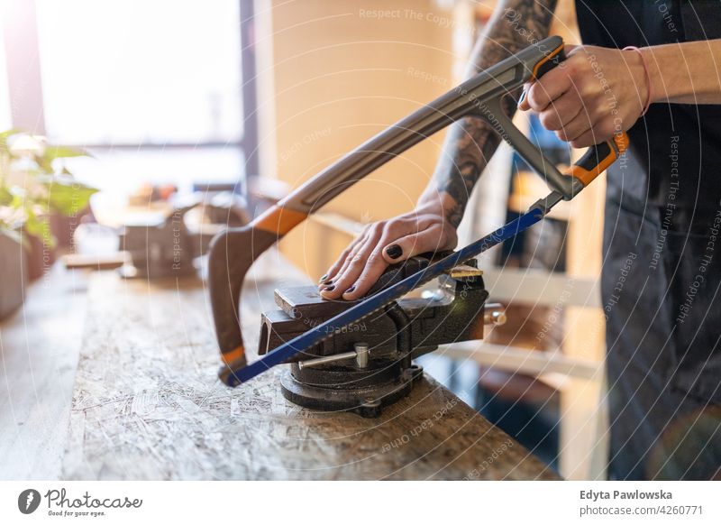 Frau mit Handsäge in ihrer Werkstatt diy Hipster farbenfroh Behaarung Tattoos Besitzer Beruf Dienst Kleinunternehmen Mitarbeiter arbeiten Techniker Arbeitsplatz