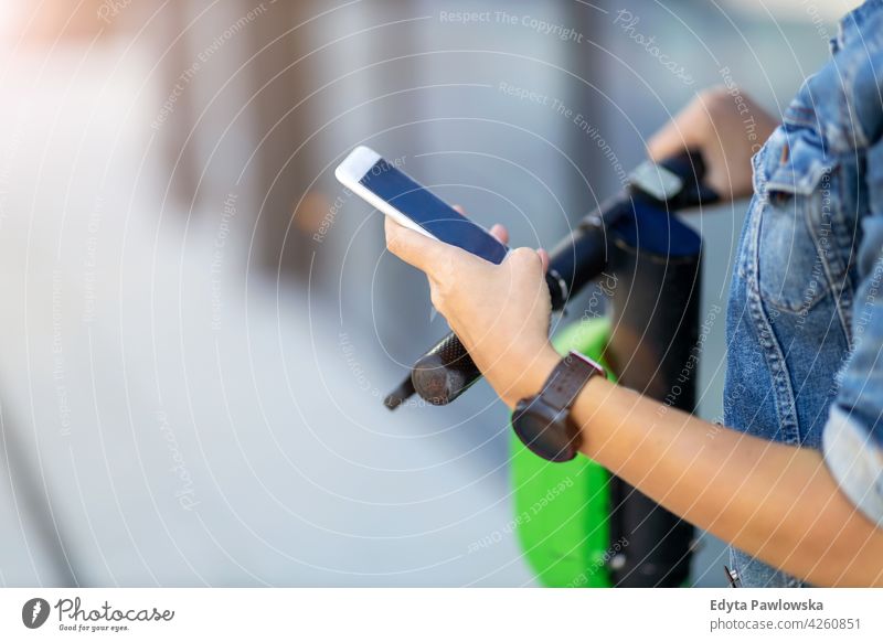 Elektroroller vom Smartphone aus aktivieren urban Straße Großstadt Menschen Frau junger Erwachsener lässig attraktiv Glück Kaukasier genießend eine Person schön