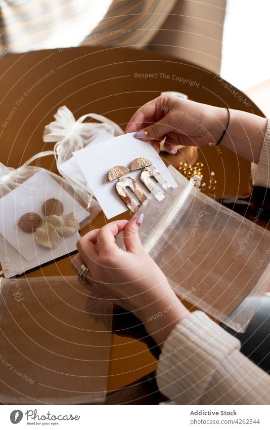 Crop gesichtslose Frau setzen handgefertigte Ohrringe auf Display-Karte Accessoire Anzeige Stil diy Kleinunternehmen Schmuck Postkarte Handwerkskunst kreieren