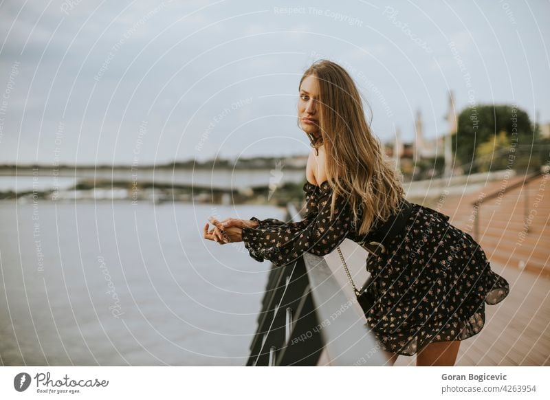 Junge lange Haare brünette Frau stehend am Flussufer allein attraktiv Tasche schön Schönheit breit Kaukasier Großstadt Tag Kleid elegant Mode Behaarung Frisur