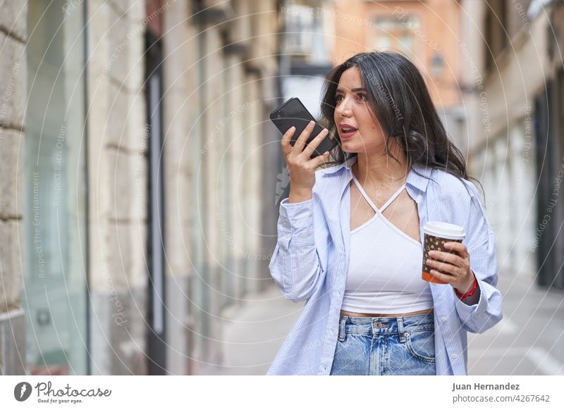 Junge Frau sendet eine Audionachricht mit Smartphone arabisch jung Senden Nachricht muslimisch Dame Handy Funktelefon ethnisch Ausdruck expressiv Kaffee Karton