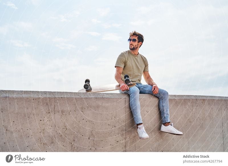 Cooler Mann mit Skateboard, der sich am Rand einer Böschung ausruht MEER Kälte Stauanlage Ufer Hafengebiet maskulin sorgenfrei sich[Akk] entspannen männlich