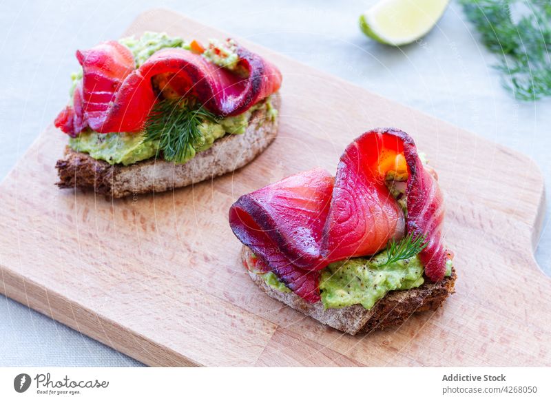 Leckere Toasts mit Guacamole und Gravlax auf dem Schneidebrett Zuprosten gravlax Amuse-Gueule Delikatesse Fisch Lachs Protein lecker geräuchert ähnlich Anlasser