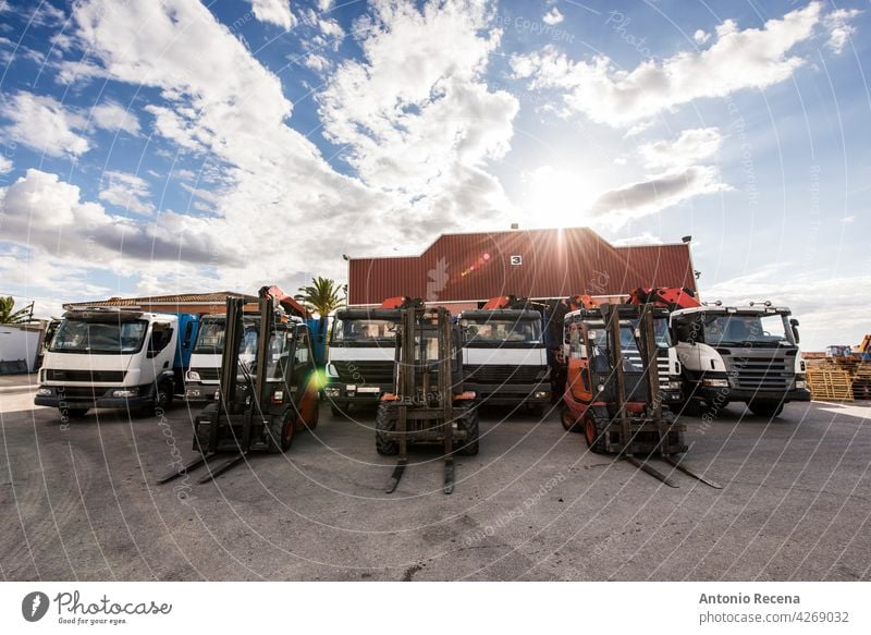 Lastwagen und Gabelstapler aufgereiht in Baufirma mit Industrielager dahinter. Weitwinkelaufnahme an einem bewölkten Tag. Konstruktion Fahrzeug Transport