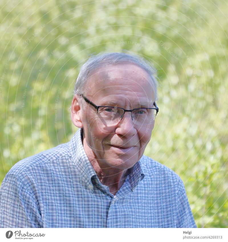 lächelnder Senior mit Brille und kurzen grauen Haaren in der Natur Mensch Mann Porträt kurzhaarig grauhaarig Lächeln Licht Schatten Hemd kariert draußen