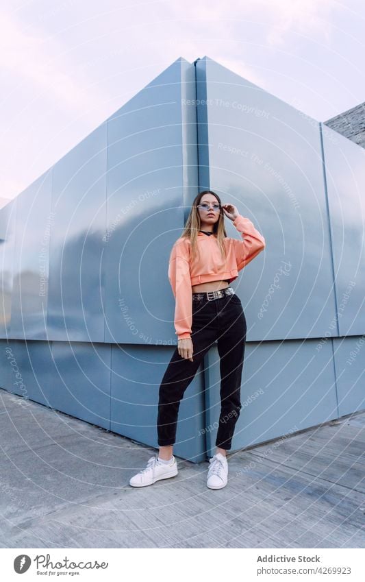 Stilvolle Frau mit Sonnenbrille lehnt an einer Hauswand cool selbstbewusst Vorschein charismatisch provokant Körperhaltung tausendjährig Youngster Jeanshose