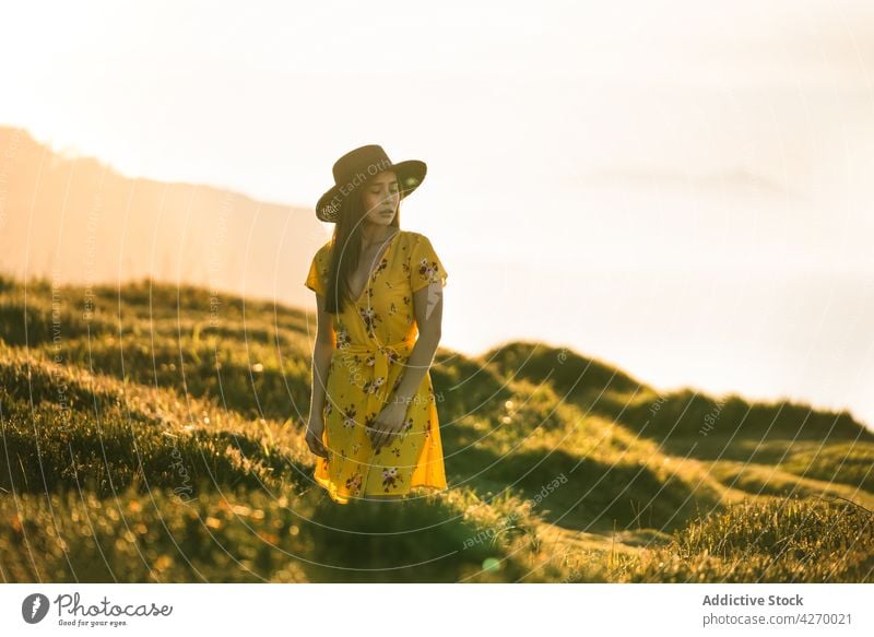 Junge Frau steht auf einem Rasenstück Sonnenkleid Landschaft Natur verträumt Grasland Wiese grasbewachsen jung Feld Hut Vorschein Gelassenheit Anmut feminin