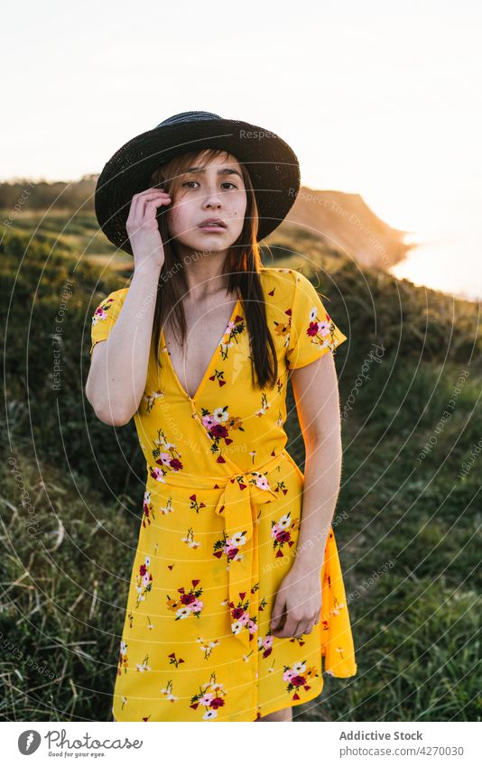 Junge Frau steht auf einem Rasenstück Sonnenkleid Landschaft Natur verträumt Grasland Wiese grasbewachsen jung Feld Hut Vorschein Gelassenheit Anmut feminin