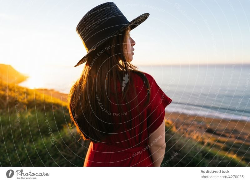 Junge Frau steht auf einem Rasenstück Sonnenkleid Landschaft Natur verträumt rot Grasland Wiese grasbewachsen jung Feld Hut Vorschein Gelassenheit Anmut feminin