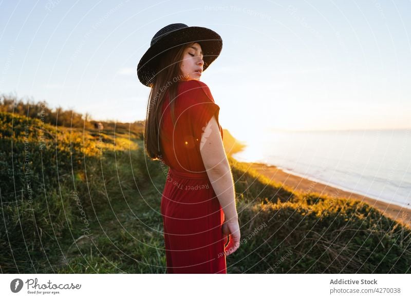 Junge Frau steht auf einem Rasenstück Sonnenkleid Landschaft Natur verträumt rot Grasland Wiese grasbewachsen jung Feld Hut Vorschein Gelassenheit Anmut feminin