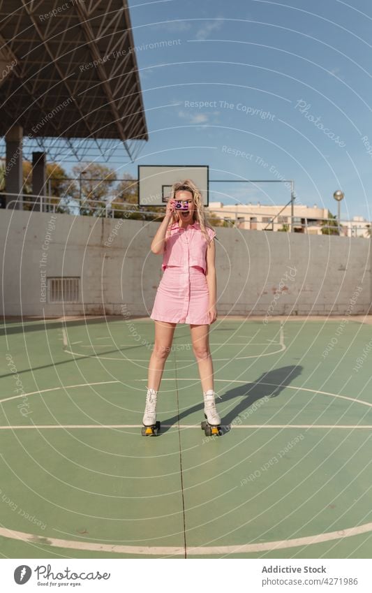 Fröhliche Frau auf Rollschuhen beim Fotografieren mit einer Sofortbildkamera Skater fotografieren Rolle heiter Sportpark Aktivität Hobby Stil Gedächtnis Freude