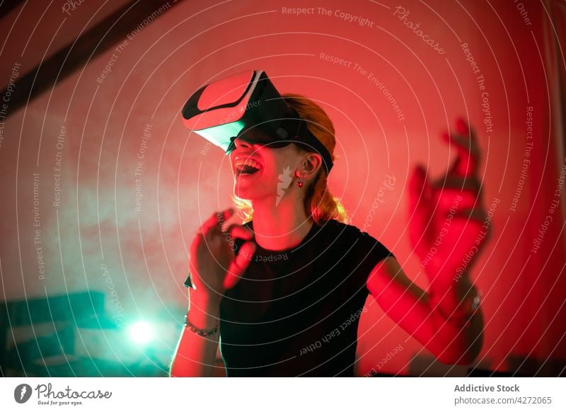 Lächelnde Frau mit VR-Brille in neonfarbenem Raum modern Headset Atelier neonfarbig Virtuelle Realität rot Licht Schutzbrille Gerät Apparatur virtuell Erfahrung