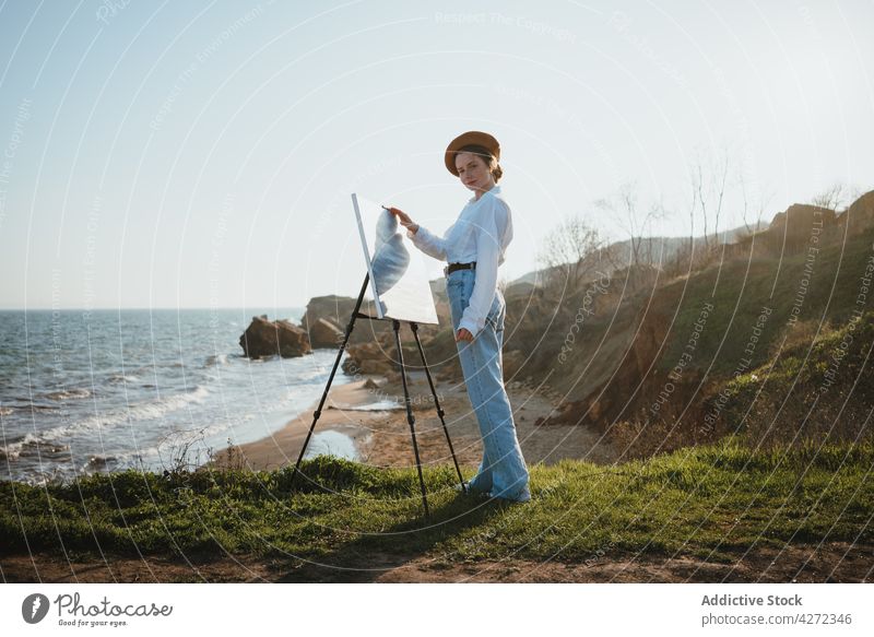 Künstlerin am Ufer bei Sand und Meer beim Malen Frau Farbe zeichnen Hobby MEER Kunst Leinwand jung Staffelei Baskenmütze kreativ Kunstwerk Stil weißes Hemd