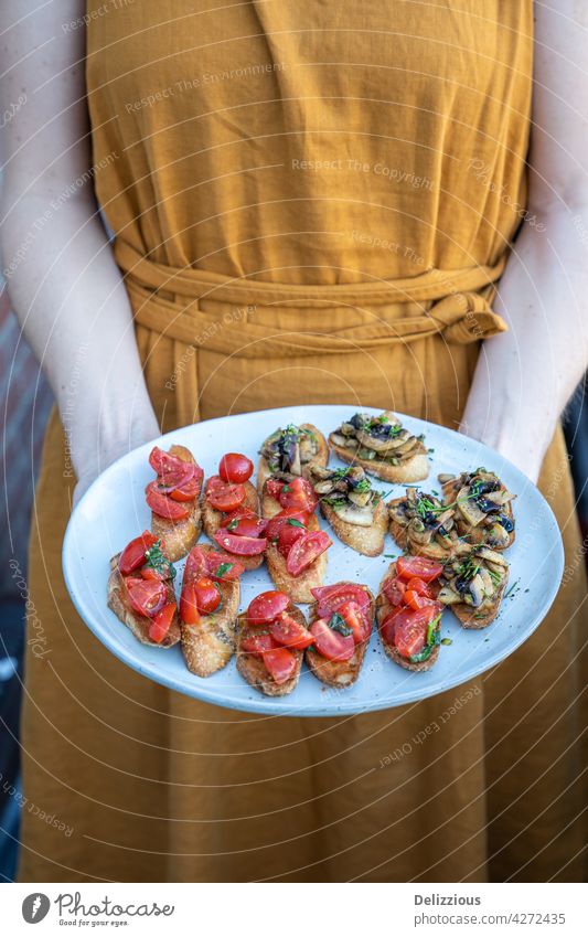 Eine Frau in einem orangefarbenen Kleid hält einen Teller mit hausgemachter Bruschetta mit Tomaten und Pilzen, Sommeressen bruchetta Snack Italienisch gebastelt