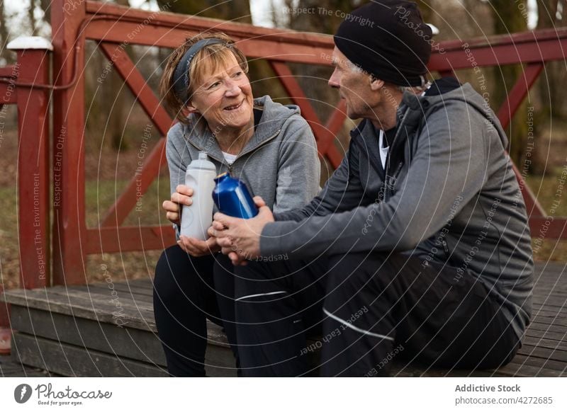 Positiv gestimmtes Paar, das nach dem Training miteinander spricht gealtert Pause Flasche sprechen Erholung Erfrischung Zusammensein positiv Mann Frau Senior