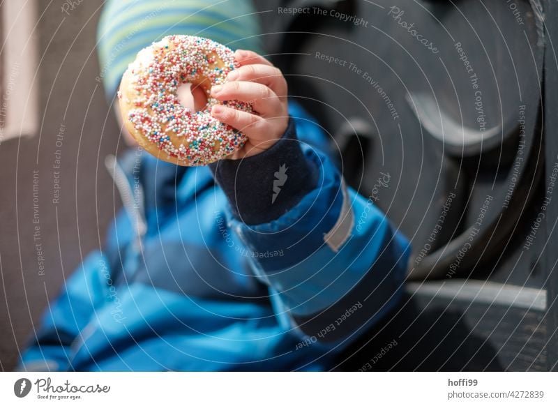 Donut mit bunten Streuseln in Kinderhand Donuts süß Süßwaren Gebäck Kuchen Zucker Backwaren lecker Dessert Lebensmittel Bäckerei Krapfen Snack rosa ungesund