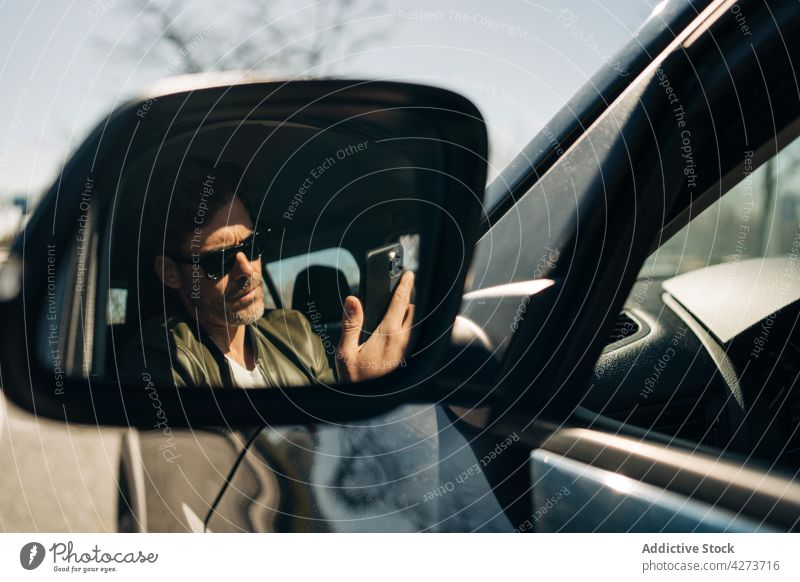 Fahrer reflektiert im Seitenspiegel, während er auf seinem Smartphone surft Browsen zuschauend Reflexion & Spiegelung PKW maskulin Sonnenbrille Mann benutzend