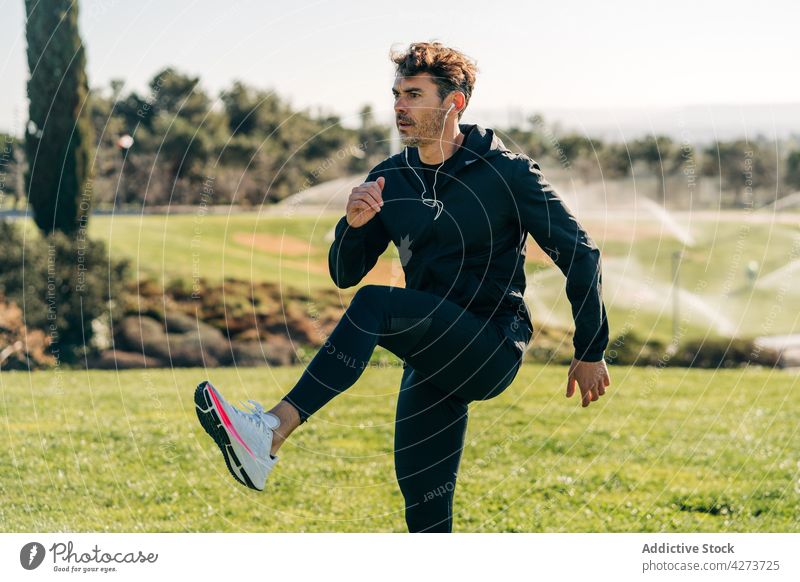 Fitnesssportler beim Training im Stadtpark Sportler Bein angehoben Übung üben Gesunder Lebensstil Aufwärmen Park Mann Energie Rasen urban Motivation Ausdauer