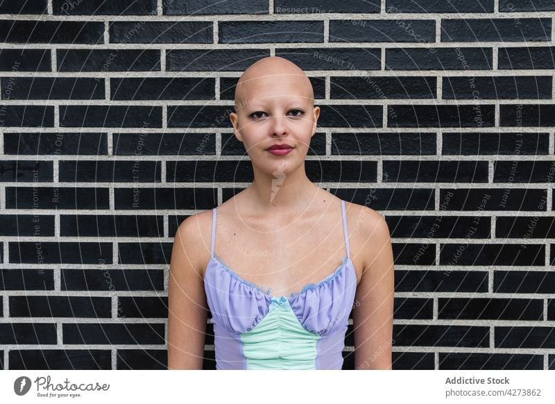 Ernste haarlose Frau in der Nähe einer Mauer stehend kahl Backsteinwand ernst allein Make-up Straße selbstbewusst Individualität Stadt jung Tageslicht feminin