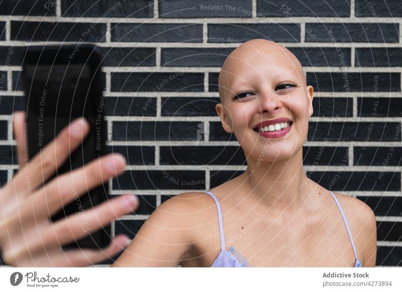 Lächelnde glatzköpfige Frau nimmt Selfie auf Telefon in der Nähe von Backsteinmauer Smartphone Backsteinwand kahl Straße modern Glück jung Gerät Mobile