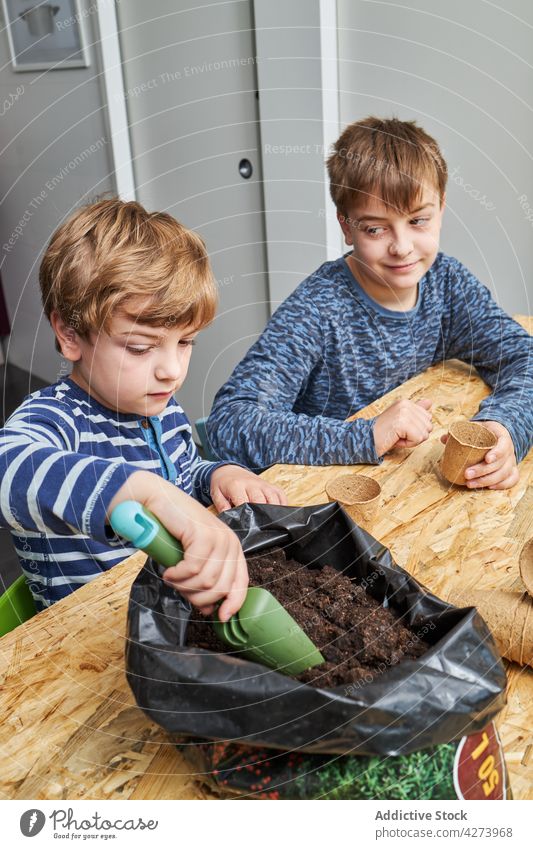 Junge mit Gartenkelle und Erde gegen Bruder zu Hause Boden Kelle Gartenarbeit Tasse umweltfreundlich Lächeln achtsam natürlich abbaubar nehmen Kinder Werkzeug