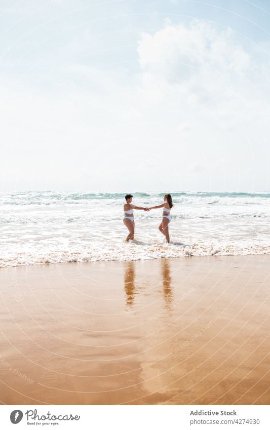 Damen im Meer stehend in der Nähe der sandigen Küste Frauen Freund Spaß haben Strand Lächeln Sand Badeanzug Blauer Himmel Glück aqua Händchenhalten Meeresufer