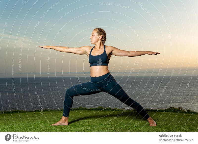 Frau Durchführung Krieger zwei Pose am Meer Ufer Yoga ausdehnen beweglich Wellness Gesunder Lebensstil Meeresufer virabhadrasana Abend Gras üben Dehnung MEER