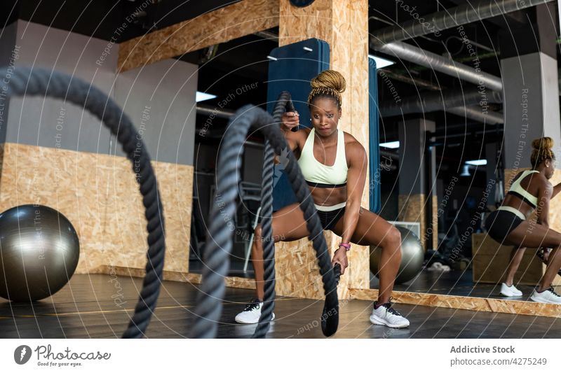 Entschlossene schwarze Sportlerin beim Training mit schweren Seilen in einer Turnhalle Schlacht operativ Fitness Motivation Stärke Herz Fitnessstudio Kraft Frau