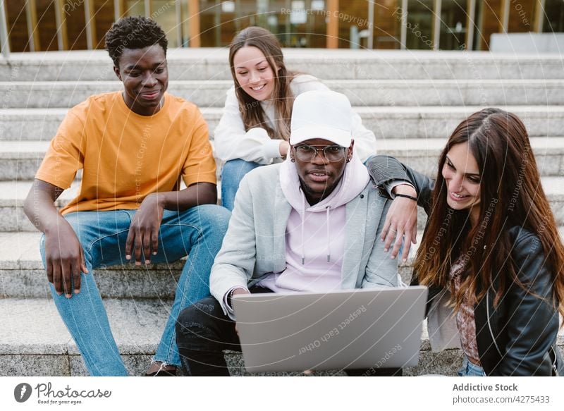 Multiethnische Studenten benutzen Laptop auf den Stufen der Universität Männer Frauen Freund zuschauen benutzend Internet teilen froh genießen männlich