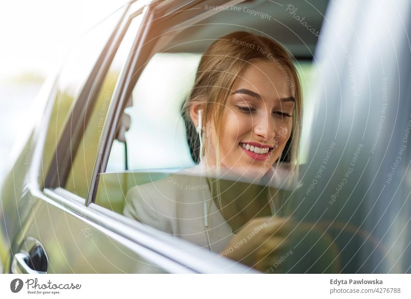 Junge Frau mit Smartphone auf dem Rücksitz eines Autos Carsharing selbstbewusst Lächeln Befriedigung attraktiv schön junger Erwachsener Freude positiv Inhalt