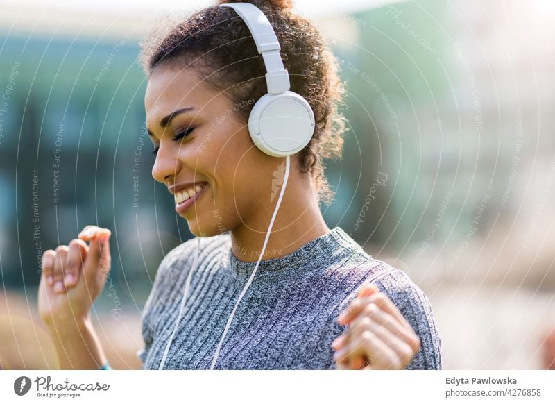 Glückliche junge Frau hört Musik in Kopfhörer in der Stadt im Freien Tag Positivität selbstbewusst sorgenfrei Menschen junger Erwachsener lässig schön attraktiv