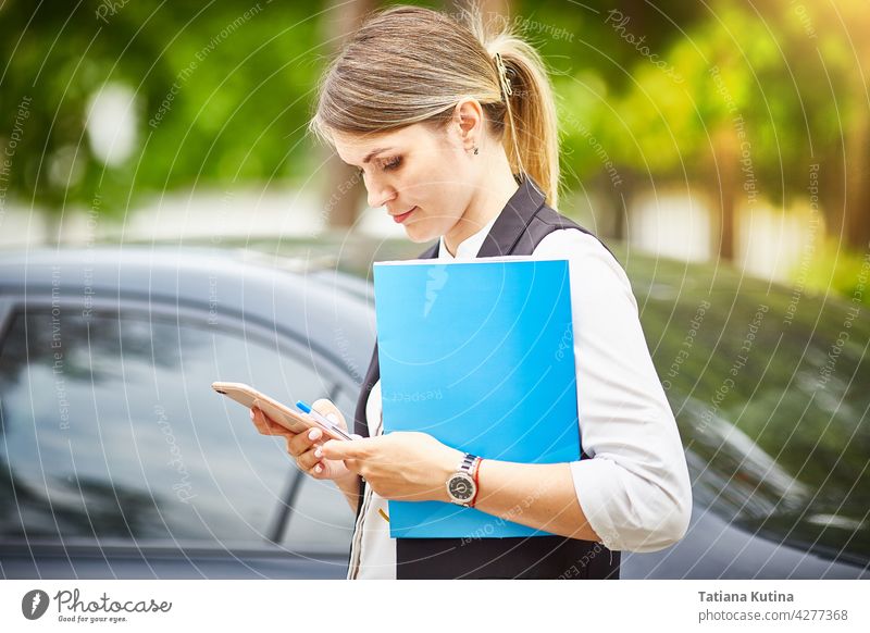 Eine junge Geschäftsfrau mit einer Mappe für Papiere in den Händen schaut auf ihr Smartphone Texten Manager Telefon Person beschäftigt professionell Büro Frau