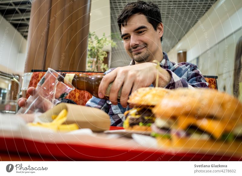 Mann isst Fastfood-Burger und trinkt Bier allein im offenen Bereich eines Restaurants in einem Einkaufszentrum Mahlzeit Lebensmittel Bar Glück Pub essen schnell