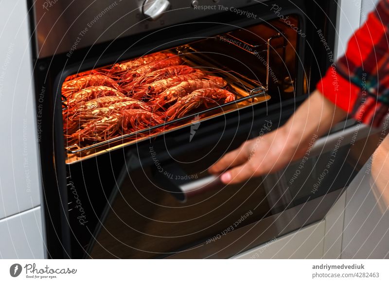 gegrillte garnelen und gebratene garnelen in der heimischen küche. frau hält einen garnelengrill auf einem rostfreien Tablett und kocht in einem elektroofen, um eine nachtparty zu feiern. meeresfrüchte