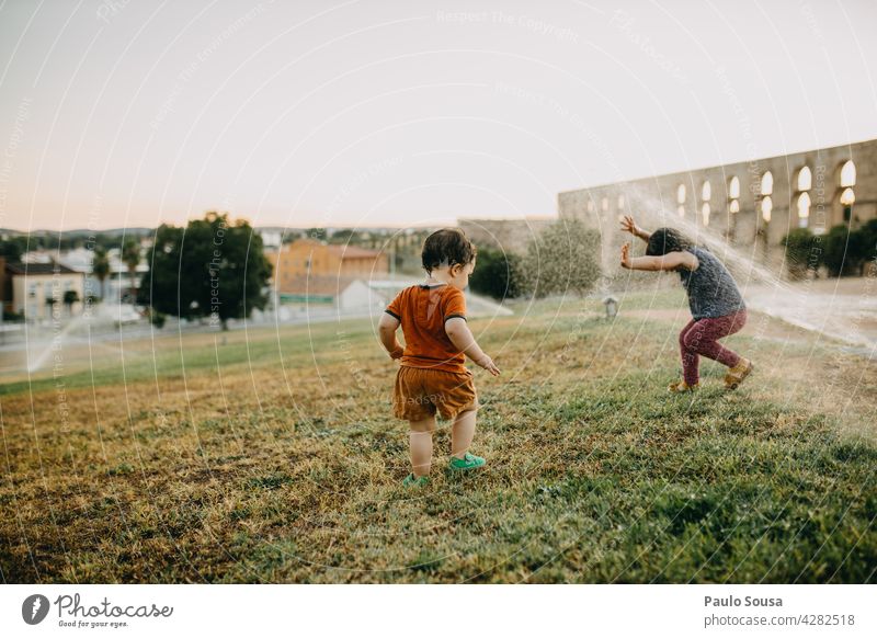 Bruder und Schwester spielen mit Wassersprinklern Geschwister Kind Sommer Erfrischung Außenaufnahme Spielen Mensch Freude Farbfoto Kindheit Junge Mädchen