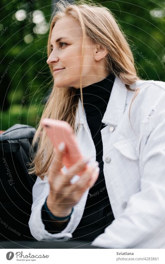 Glückliche Blondine sitzt auf einer Bank in einem Stadtpark, telefoniert und schreibt SMS mit Freunden Park Frau Lifestyle jung Menschen Mobile Mitteilung