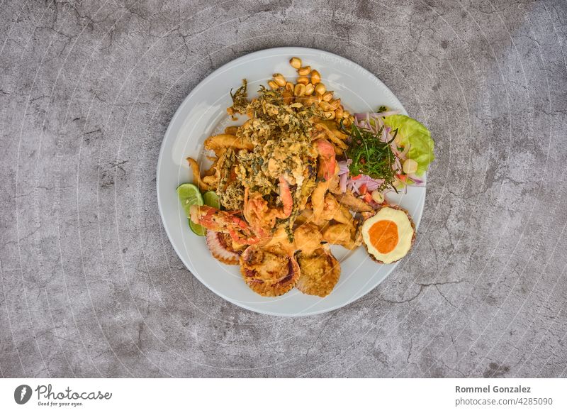 Peruanisches Essen: Jalea de pescado oder Fischkrapfen mit gebratenem Maniok und Zwiebelsalat mit Chili, serviert auf einem weißen Teller. Gebratene Meeresfrüchte