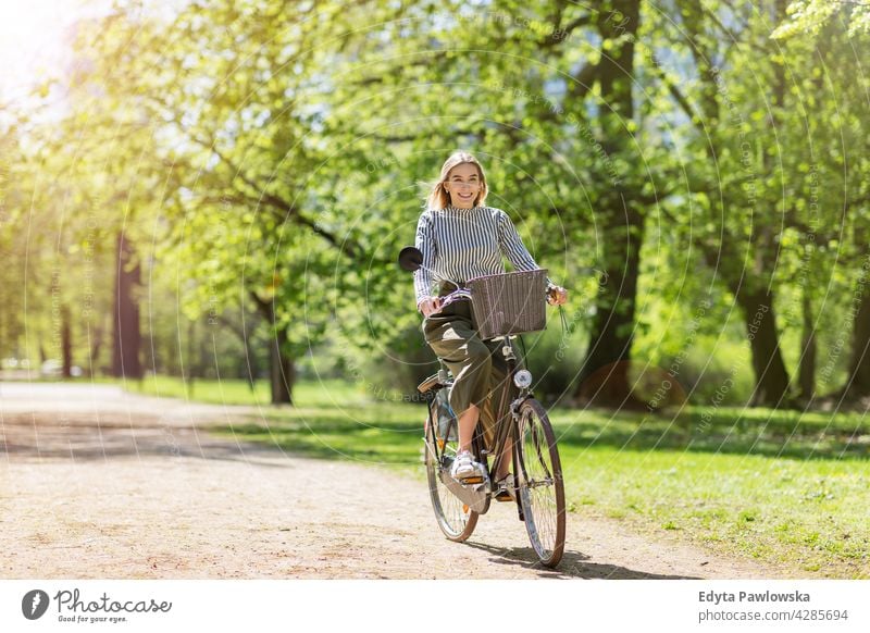 Junge Frau radelt durch den Park grün Bäume Natur Frische genießend Lifestyle jung Erwachsener Menschen lässig Kaukasier positiv Glück Lächeln attraktiv schön