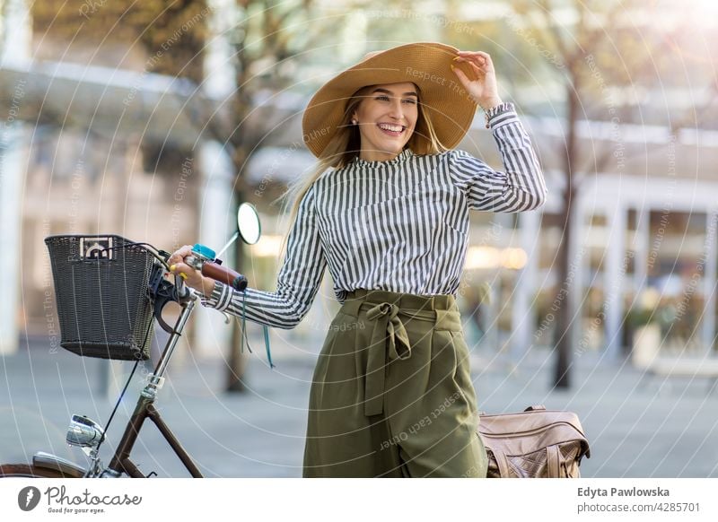 Junge Frau steht mit ihrem Fahrrad in der Stadt Strohhut Feiertag Urlaub Mode Park grün Bäume Natur Frische genießend Lifestyle jung Erwachsener Menschen lässig