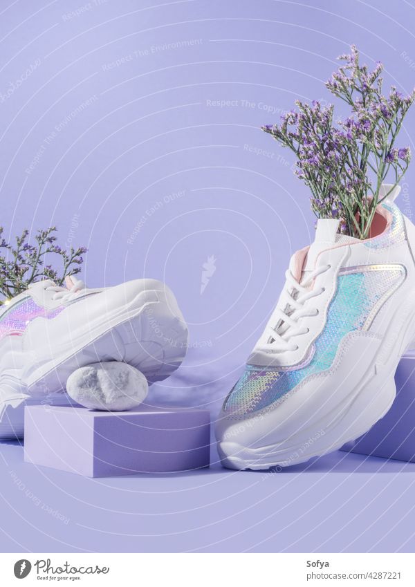 Weiße weibliche Turnschuhe mit Pailletten mit Blumen innen auf lila Hintergrund mit geometrischen Würfel Podium Schuhe Mode Frau purpur Spaziergang urban Natur