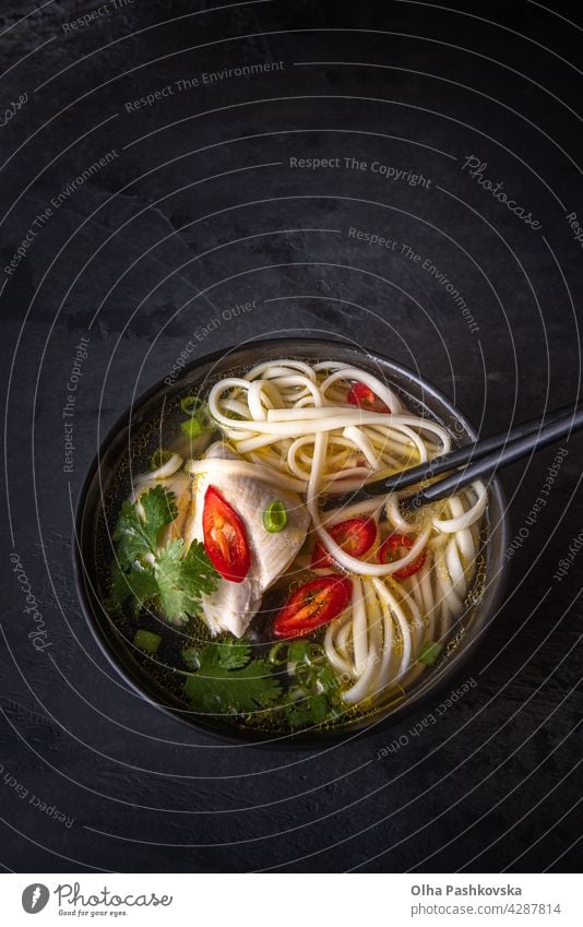 Asiatische Suppe und Essstäbchen mit Kopierraum auf Schwarz oben Frühlingszwiebeln Nahaufnahme Suppenteller vertikal Hähnchen stylisch Oberfläche Stein