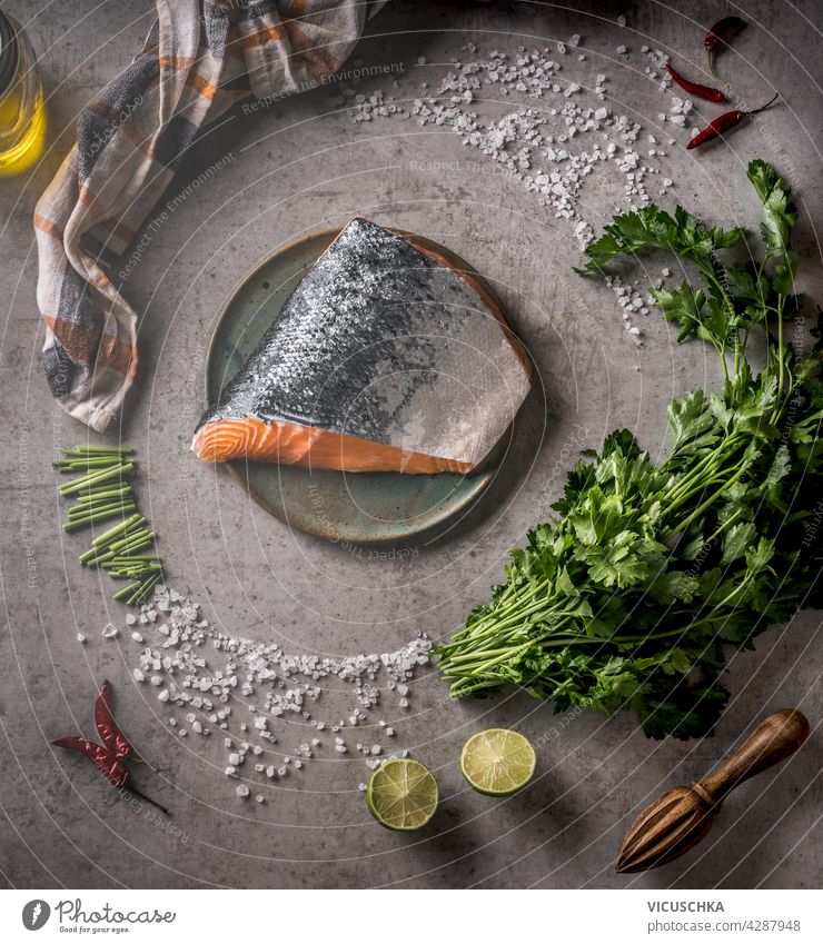 Roher Lachs mit Chili, Salz und Zitrone. Kreisförmige Zutaten und Küchengeräte. Grauer Beton-Hintergrund. Ansicht von oben. Gesundes Meeresfrüchte-Konzept