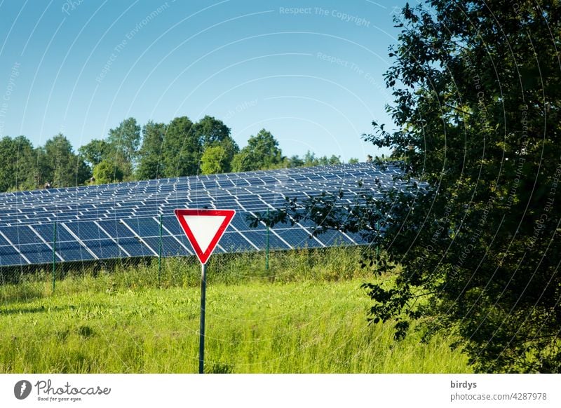 Vorfahrt achten - Schild vor einem Solarpark umgeben von Bäumen und Wiese. Symbolbild, vorrangig regenerative Energien fördern. Solarförderung Photovoltaik