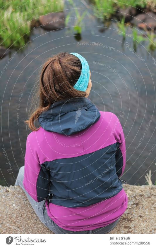 Junge Frau in sportlicher Kleidung sitzt auf einer Brücke am Bach sitzen Beton lange Haare braune Haare brünett Pferdeschwanz lila pink Natur Naturschutzgebiet