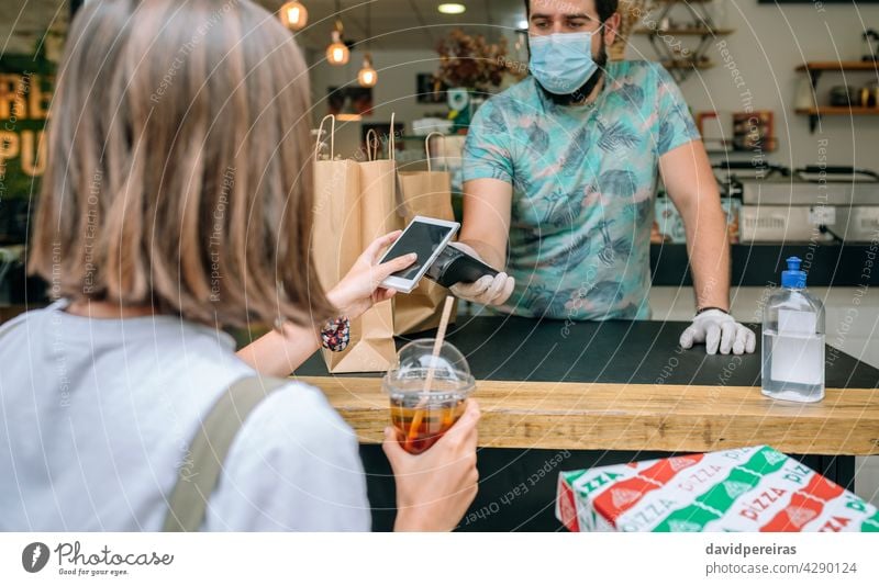 Frau, die mit dem Handy eine Bestellung zum Mitnehmen bezahlt bezahlen wegnehmen nfc Pos-Terminal Coronavirus Lebensmittel-Lieferung trinken Schutzmaske