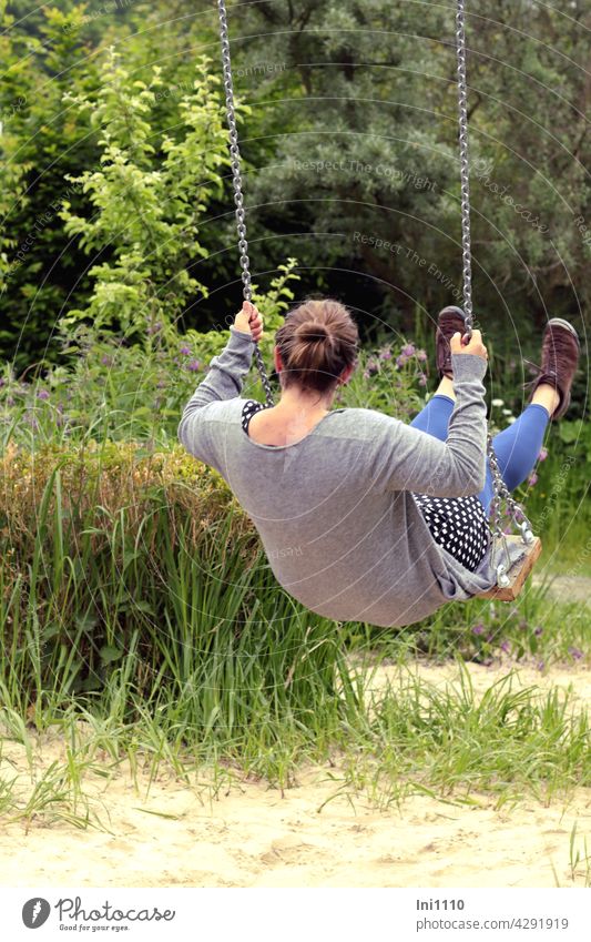 junge Frau mit Dutt Frisur schaukelt im Garten Erwaschene Rücken Rückenansicht Strickjacke Pünktchenkleid blaue Leggins braune Schuhe Schaukel schaukeln