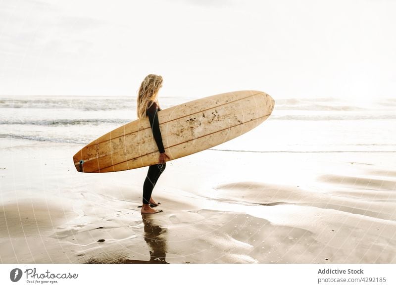 Weibliche Surferin am Strand mit Surfbrett stehend Frau Natur Sonnenuntergang winken im Freien Neoprenanzug Meeresküste Brandung Sportlerin MEER Surfen Hobby