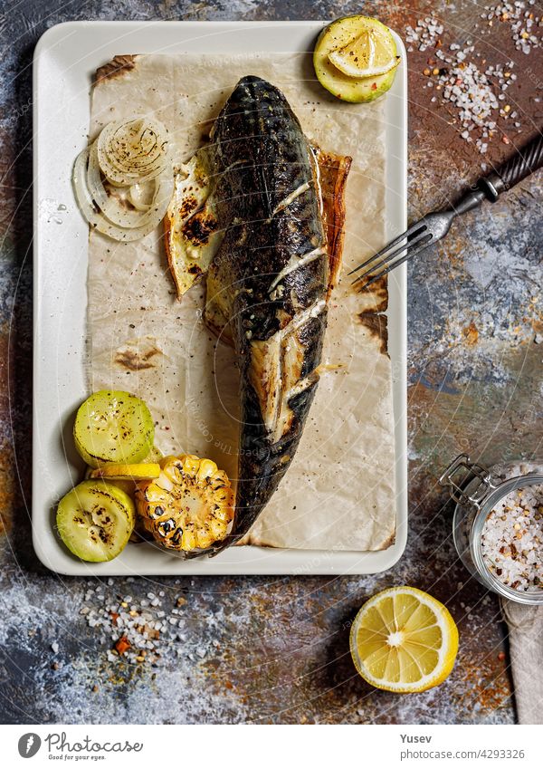 Draufsicht köstliche gegrillte Makrele mit Gemüse auf einer rechteckigen Platte. Appetitlicher gebratener Seefisch mit Mais, Zucchini und gewürzter Zitrone. Mediterrane Küche. Gesunde Meeresfrüchte. Vertikale Aufnahme