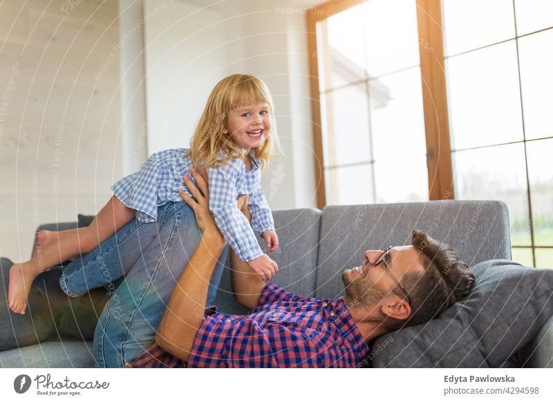 Glücklicher Vater spielt mit Tochter auf Sofa zu Hause heimwärts Mann Papa Familie Eltern Verwandte Kind Mädchen kleines Mädchen Kinder Partnerschaft